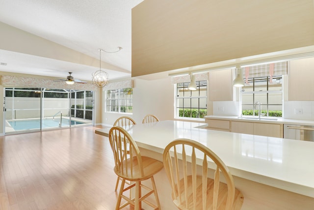 dining area featuring light hardwood / wood-style flooring, sink, ceiling fan with notable chandelier, and lofted ceiling