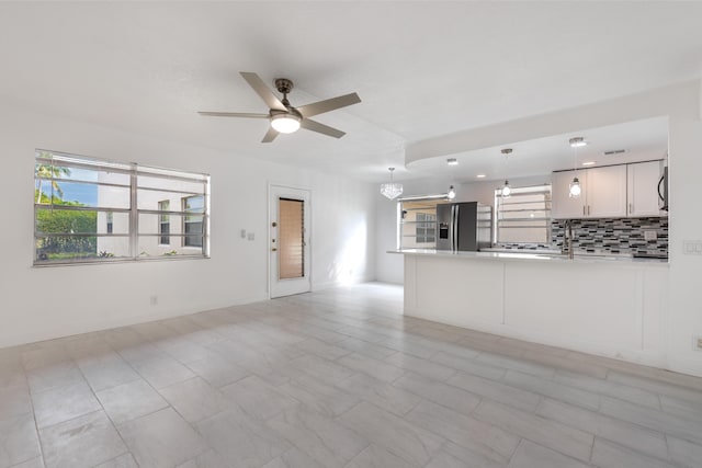 unfurnished living room with ceiling fan with notable chandelier