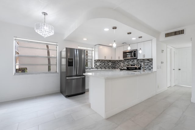 kitchen featuring stainless steel appliances, a notable chandelier, kitchen peninsula, pendant lighting, and white cabinets