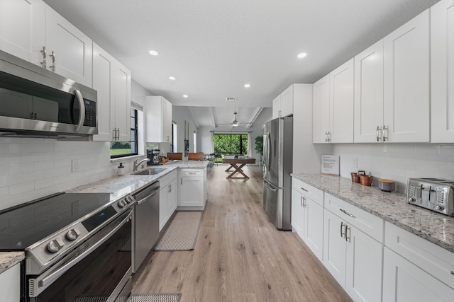 kitchen with stainless steel appliances, white cabinets, light stone countertops, light hardwood / wood-style floors, and tasteful backsplash