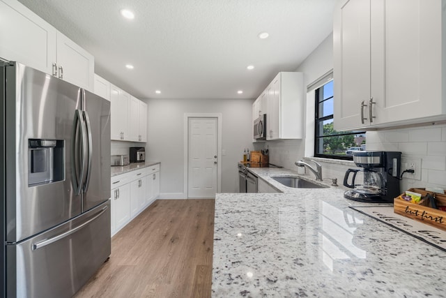 kitchen featuring light wood-type flooring, stainless steel appliances, white cabinetry, backsplash, and light stone counters