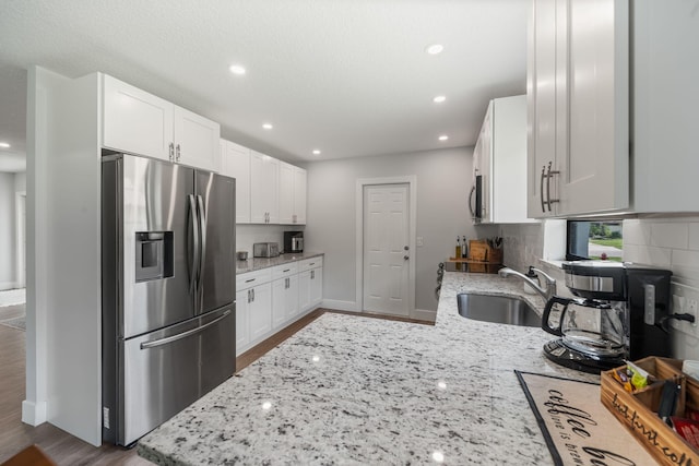 kitchen featuring stainless steel appliances, decorative backsplash, hardwood / wood-style floors, light stone countertops, and sink