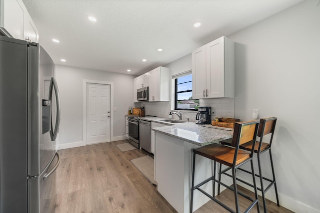 kitchen featuring appliances with stainless steel finishes, a breakfast bar area, white cabinets, light hardwood / wood-style floors, and light stone counters