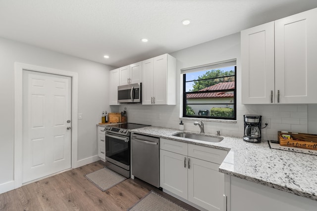 kitchen with stainless steel appliances, sink, backsplash, white cabinetry, and light hardwood / wood-style flooring