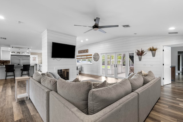 living room with ceiling fan, a large fireplace, dark wood-type flooring, and wood walls