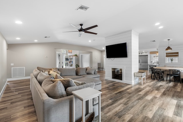 living room with ceiling fan, a large fireplace, and dark wood-type flooring