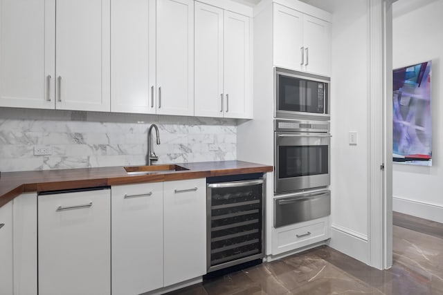 kitchen with butcher block counters, sink, beverage cooler, white cabinets, and appliances with stainless steel finishes