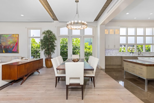 dining room with light wood-type flooring, crown molding, sink, beamed ceiling, and a chandelier