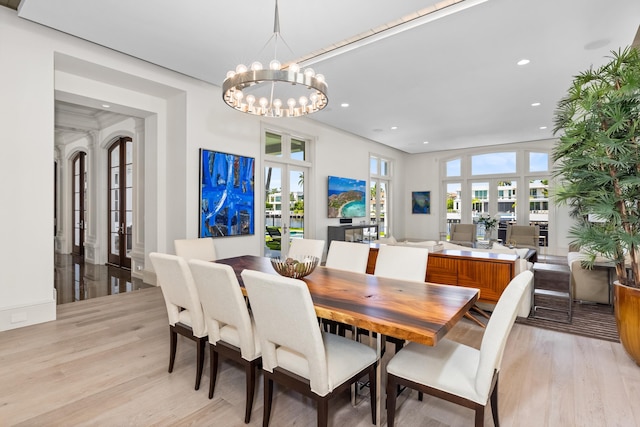 dining space with french doors, light wood-type flooring, and a notable chandelier