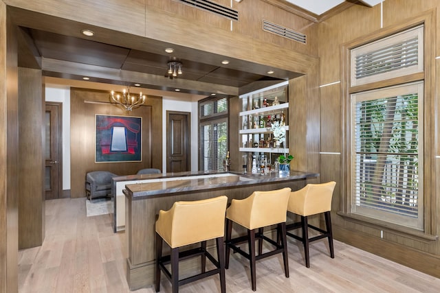 bar featuring pendant lighting, light wood-type flooring, wooden walls, and a notable chandelier