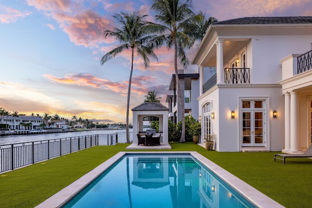 pool at dusk with a lawn, a patio area, and a water view