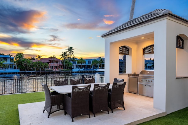 patio terrace at dusk featuring a grill and exterior kitchen