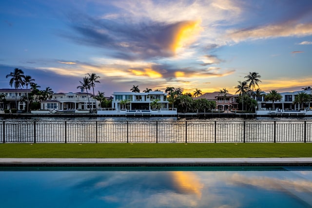 pool at dusk featuring a yard and a water view