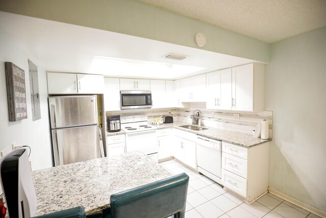 kitchen with light tile patterned floors, appliances with stainless steel finishes, sink, tasteful backsplash, and white cabinetry