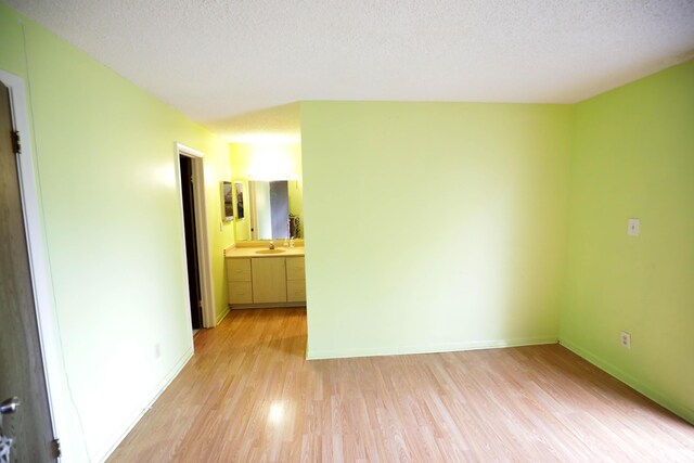 unfurnished bedroom with ensuite bath, sink, light hardwood / wood-style flooring, and a textured ceiling