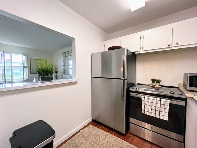 kitchen with appliances with stainless steel finishes, white cabinets, and hardwood / wood-style floors