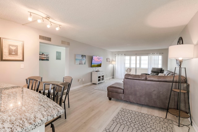 living room featuring rail lighting, a textured ceiling, and light hardwood / wood-style flooring