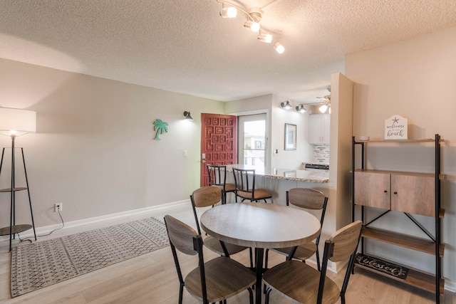 dining space featuring ceiling fan, light hardwood / wood-style floors, track lighting, and a textured ceiling