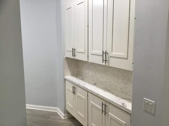 interior space featuring decorative backsplash, light stone countertops, dark hardwood / wood-style flooring, and white cabinets