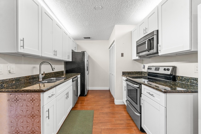 kitchen featuring sink, light hardwood / wood-style flooring, dark stone counters, white cabinets, and appliances with stainless steel finishes