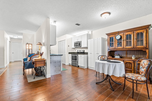 kitchen with white cabinetry, dark hardwood / wood-style flooring, stainless steel appliances, and a textured ceiling