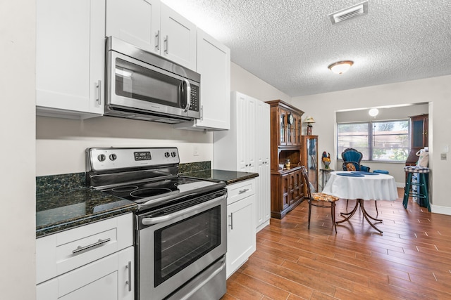 kitchen featuring white cabinets, appliances with stainless steel finishes, light hardwood / wood-style flooring, and dark stone counters