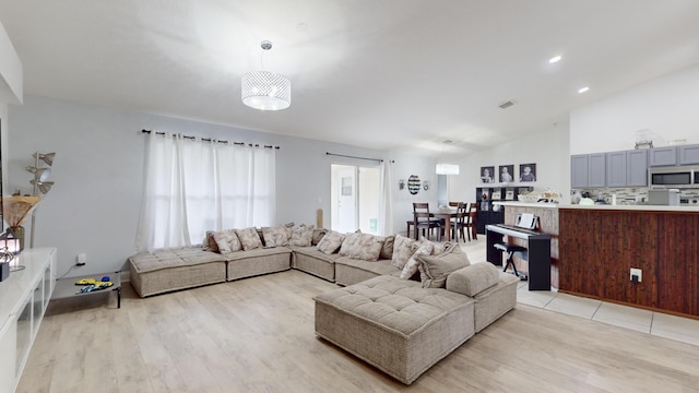 living room with vaulted ceiling, a notable chandelier, and light wood-type flooring