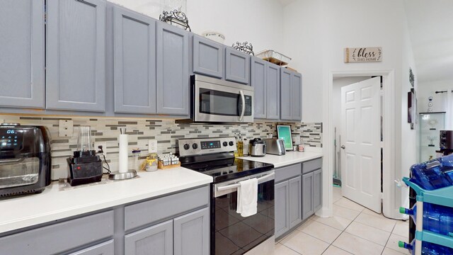 kitchen with gray cabinets, light tile patterned floors, decorative backsplash, and stainless steel appliances