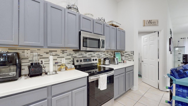 kitchen with light tile patterned floors, gray cabinets, stainless steel appliances, light countertops, and backsplash