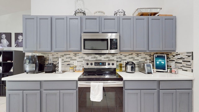 kitchen with appliances with stainless steel finishes, lofted ceiling, tasteful backsplash, and gray cabinetry