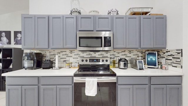 kitchen with gray cabinets, decorative backsplash, stainless steel appliances, and light countertops