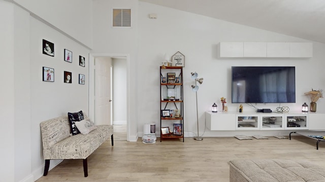 living area featuring vaulted ceiling, light wood-type flooring, visible vents, and baseboards