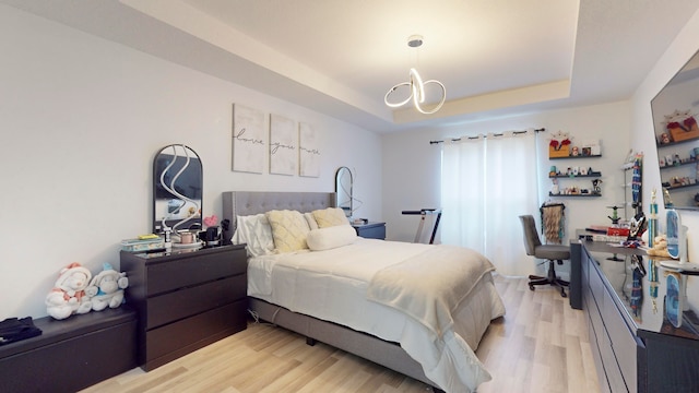 bedroom with an inviting chandelier, light wood-type flooring, and a tray ceiling