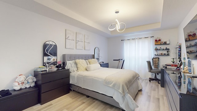 bedroom with light wood-style floors, a raised ceiling, and a notable chandelier