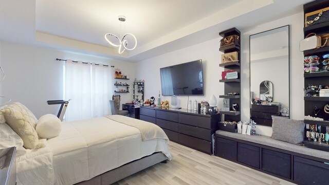 bedroom featuring an inviting chandelier, light wood-type flooring, and a raised ceiling