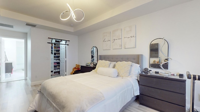 bedroom with a raised ceiling, visible vents, and light wood-style floors