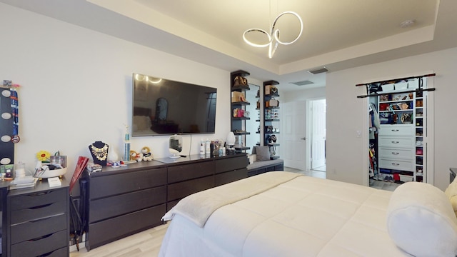 bedroom featuring light wood finished floors, a spacious closet, visible vents, and a raised ceiling