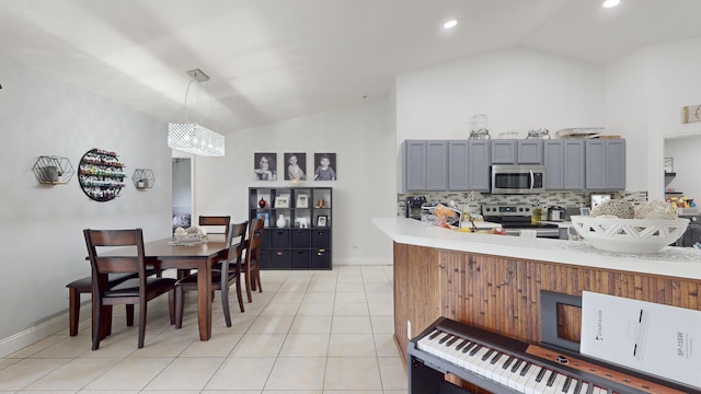 kitchen with decorative light fixtures, stainless steel appliances, gray cabinets, light countertops, and vaulted ceiling