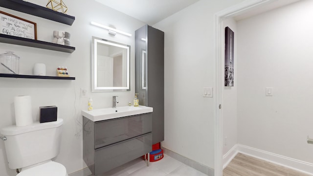 half bath featuring toilet, wood finished floors, vanity, and baseboards