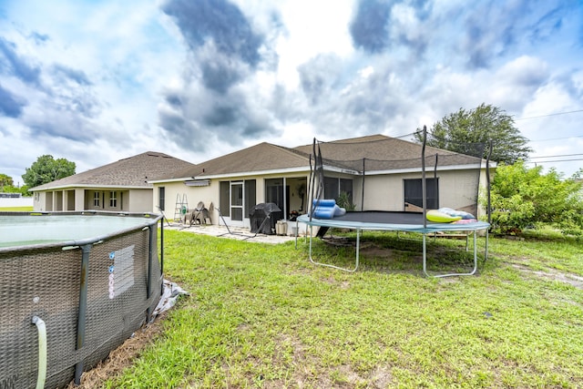 rear view of house with a trampoline, an outdoor pool, a lawn, and stucco siding