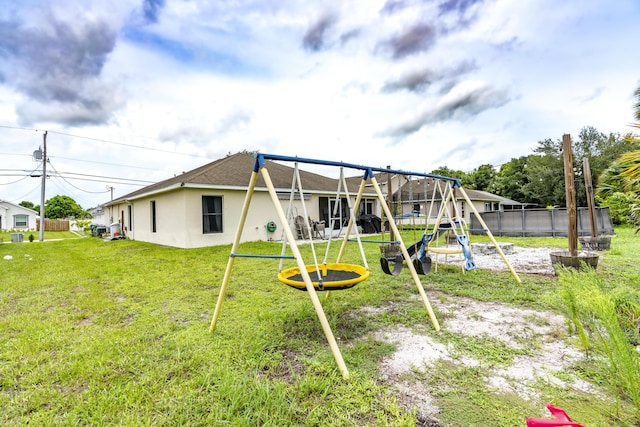 rear view of property with a lawn, a trampoline, fence, a playground, and stucco siding