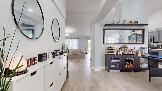 bar with tasteful backsplash, light wood-type flooring, and stainless steel microwave