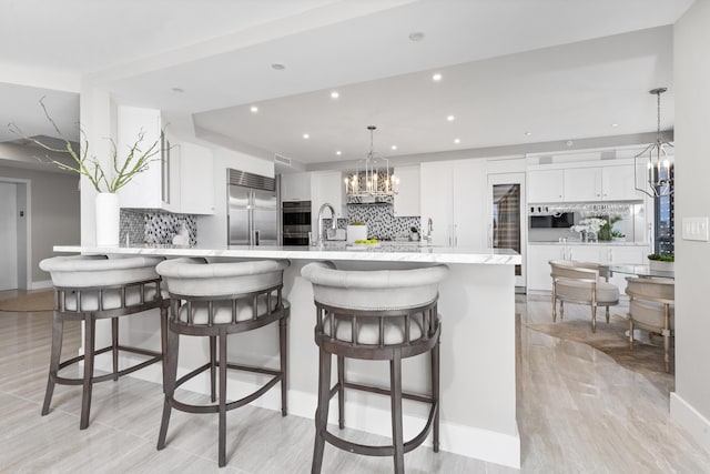 kitchen featuring white cabinetry, a breakfast bar area, backsplash, hanging light fixtures, and appliances with stainless steel finishes