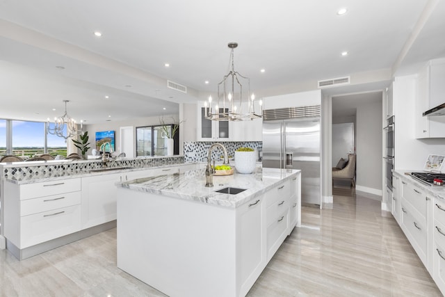 kitchen with tasteful backsplash, light stone counters, hanging light fixtures, a large island with sink, and sink