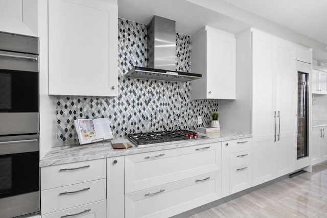 kitchen featuring white cabinets, backsplash, wall chimney exhaust hood, and double oven