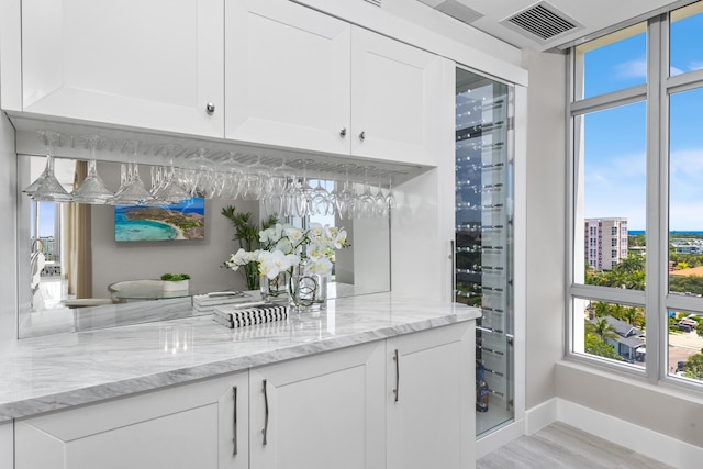 bar with white cabinets, light stone counters, and light wood-type flooring