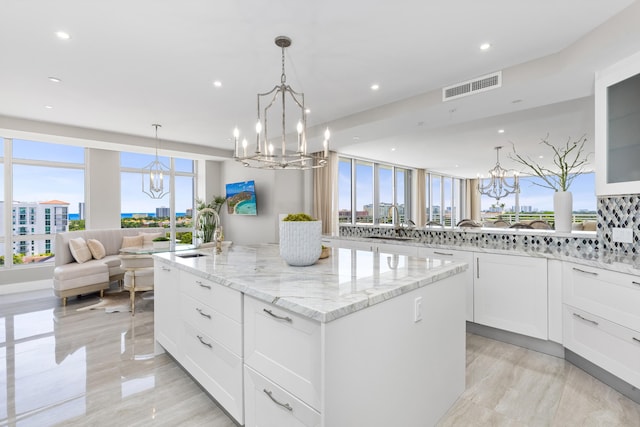 kitchen with light stone counters, hanging light fixtures, a healthy amount of sunlight, a kitchen island, and white cabinetry