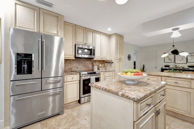 kitchen featuring a kitchen island, appliances with stainless steel finishes, cream cabinets, hanging light fixtures, and light stone countertops