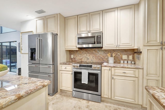 kitchen with light stone counters, cream cabinets, backsplash, and stainless steel appliances