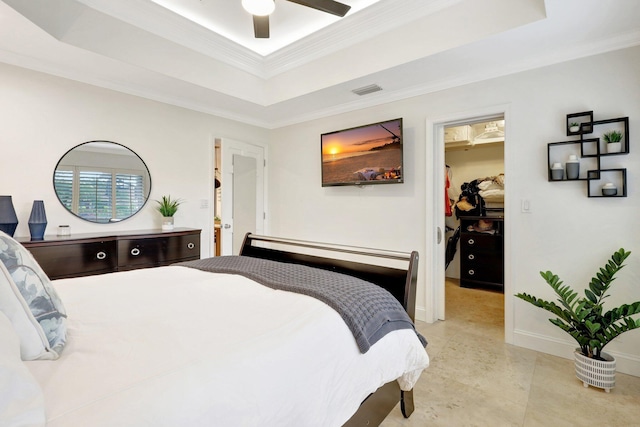 bedroom with crown molding, a walk in closet, a raised ceiling, and ceiling fan